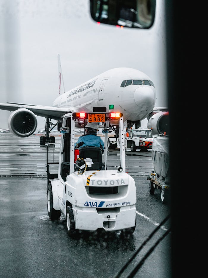 Airport ground crew operating a vehicle in front of a parked airliner on a rainy runway.
